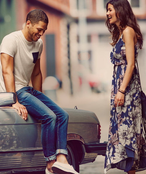 Woman laughing with a man sitting on a car